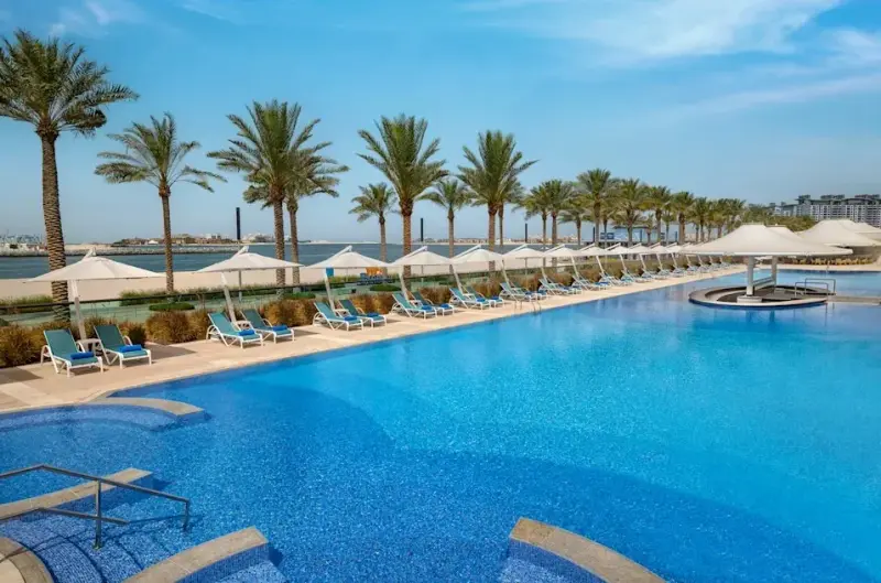 Бассейн Hilton Dubai Palm Jumeirah с шезлонгами и пальмами у моря